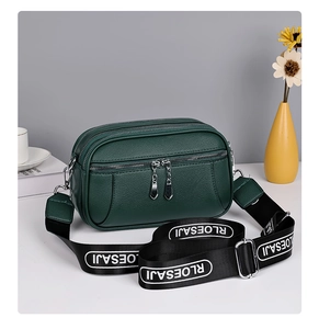 Detail of dark green pebble leather bag with triple zippers and woven letter strap