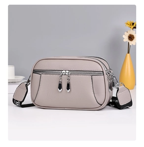 Detail of grey pebbled leather crossbody bag with multiple zippers and wide fabric strap