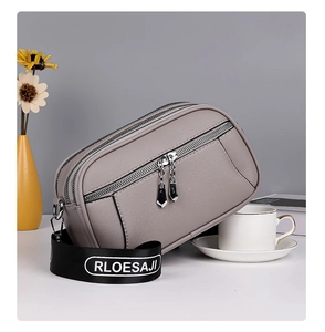 Detail of gray leather crossbody bag with triple zippers and logo wide strap on desk