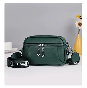 Close-up of dark green textured leather crossbody bag with wide woven strap and silver zippers