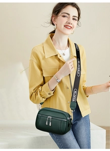Detail of dark green leather crossbody bag with wide logo strap and double zippers