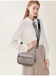 Detailed view of grey pebbled leather crossbody bag with multi-layer zippers and wide strap