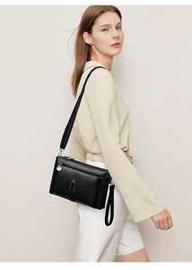 Close-up of minimalist black leather crossbody bag styled on a light outfit