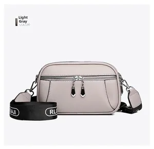 Detail of light gray lychee grain leather crossbody bag with dual zippers and woven strap
