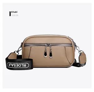 Detail view of khaki pebbled leather crossbody bag with dual zippers and logo wide strap