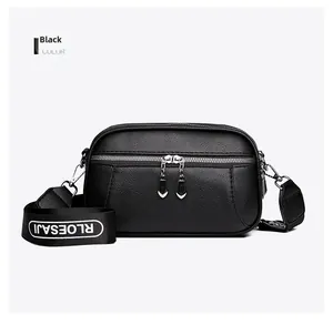 Detail of black pebbled leather crossbody bag with dual zippers and woven letter strap