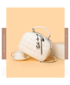 Detail of quilted white crossbody bag with silver bear charm and chain strap
