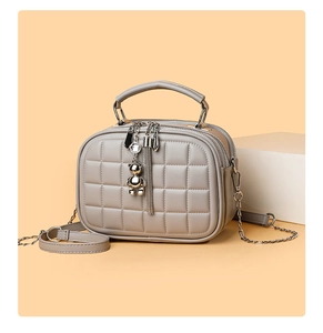 Detail of grey quilted crossbody bag with metal chain strap and decorative bear tassel
