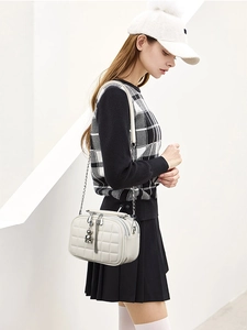 Detail of cream quilted crossbody bag with three zipper layers and silver chain strap