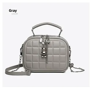 Detail of grey quilted handbag featuring dual zippers, top handle and metal bear charm