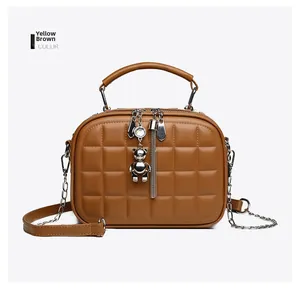 Detail of tan quilted round crossbody bag with silver bear pendant and chain strap