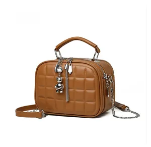 Detail of caramel quilted mini bag with silver bear charm and tassel on white background