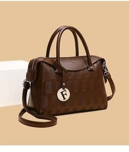 Détail d'un sac à main marron foncé avec relief tressé, pendentif F et bandoulière