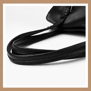 Dettaglio dei robusti doppi manici in pelle e degli inserti in metallo nero della borsa
