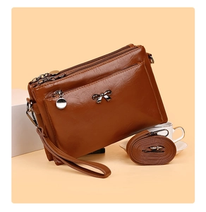 Detail einer dunkelbraunen Handtasche mit drei Reißverschlüssen und eleganter Metallschleife