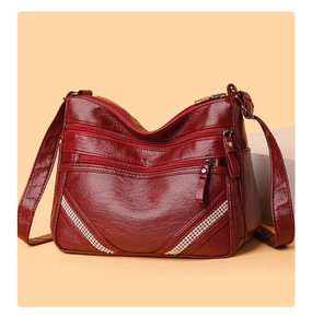 Dettaglio borsa in pelle bordeaux con cerniere multiple e decoro a V in strass