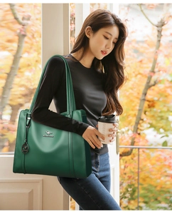 Dettaglio borsa tote in pelle verde scuro con logo metallico e ciondolo alla moda