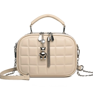 Beige quilted crossbody bag with top handle and bear charm on white background