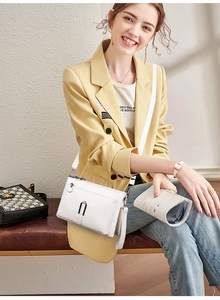 Detail of white cross-body bag with U-shaped metal hardware on model in yellow blazer