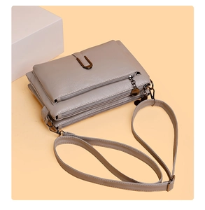 Close-up of taupe crossbody bag featuring three zipper compartments and a U-shaped metal buckle