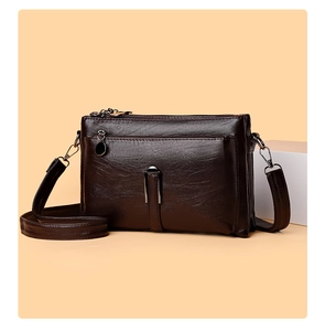 Detail of dark brown leather crossbody bag featuring multiple zippers and pebble texture