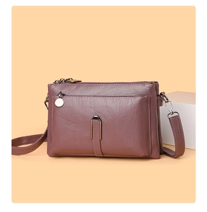 Detail of dark purple leather crossbody bag featuring multi-layer zippers and metal hardware