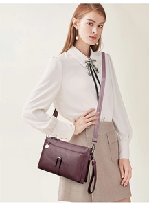 Detail of burgundy textured leather crossbody bag with silver zippers and shoulder strap