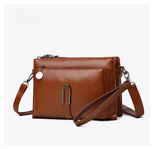 Detail view of brown faux leather crossbody bag with multiple zippers and metal buckle