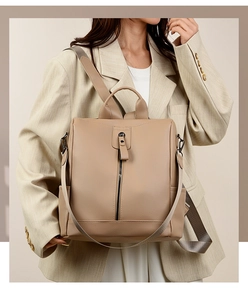 Detail of beige textured leather backpack featuring vertical zip and woven strap on model