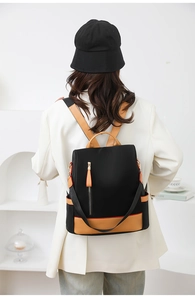 Detail of female model wearing the black nylon backpack with brown leather trim and back zipper