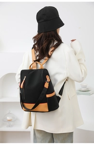 Detailed back view of a black nylon backpack with brown leather trim on a female model