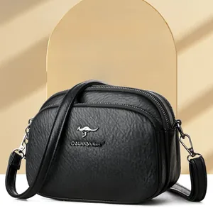 Detail of black pebbled leather crossbody bag with three zipper compartments and gold logo