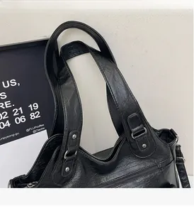 Detail view of black PU leather shoulder bag with sturdy handles and silver metal rivets