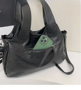 Detail of a black faux leather tote bag showing a back zipper pocket with a smartphone