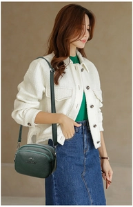 Detail of dark green pebble leather shoulder bag featuring dual zippers and metal logo