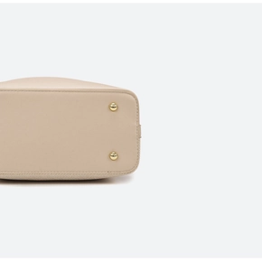 Detail view of reinforced stitching and gold metal protective studs on beige handbag base
