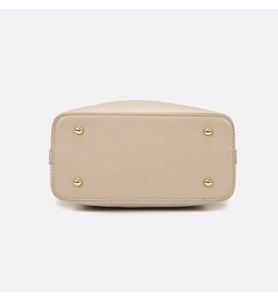 Close-up of beige handbag bottom featuring four gold metal protective feet and neat stitching