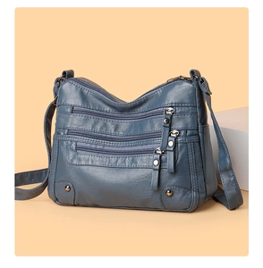 Detail view of matte blue-grey multi-pocket shoulder bag with zippers and metal studs