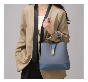 Detail of blue canvas bucket bag with gold clasp and smooth leather base worn by a model