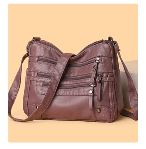 Detail of wine red soft leather crossbody bag with multiple zip pockets and metal accents