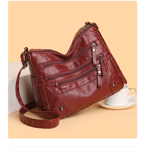 Detail view of dark red soft leather crossbody bag with multiple zip pockets and metal studs