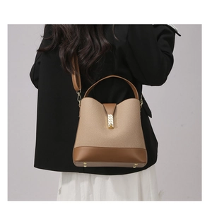 Detail view of beige canvas bucket bag with brown leather trim and metallic buckle