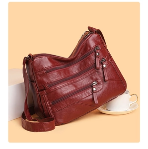 Detail view of wine red soft leather shoulder bag with multiple zippered pockets
