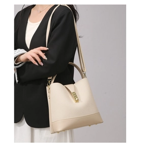 Detail of beige canvas bucket bag with smooth leather trim and golden metal clasp