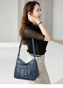 Detail view of a navy blue woven crossbody bag with multiple zippers and soft leather texture