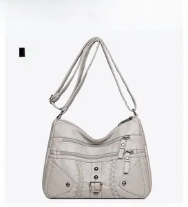 Detail view of the beige woven crossbody bag with multiple zippers and metallic studs