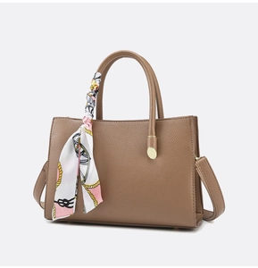 Detail of tan pebble leather tote with dual handles, gold hardware and decorative silk scarf