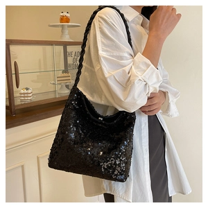 Detail of black sequined crescent tote with thick woven shoulder strap on model