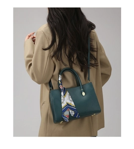 Detail of dark green lychee leather handbag with silk scarf on handle and gold studs