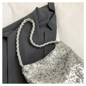Detailed view of silver sequin handbag with twisted handle on black blazer background
